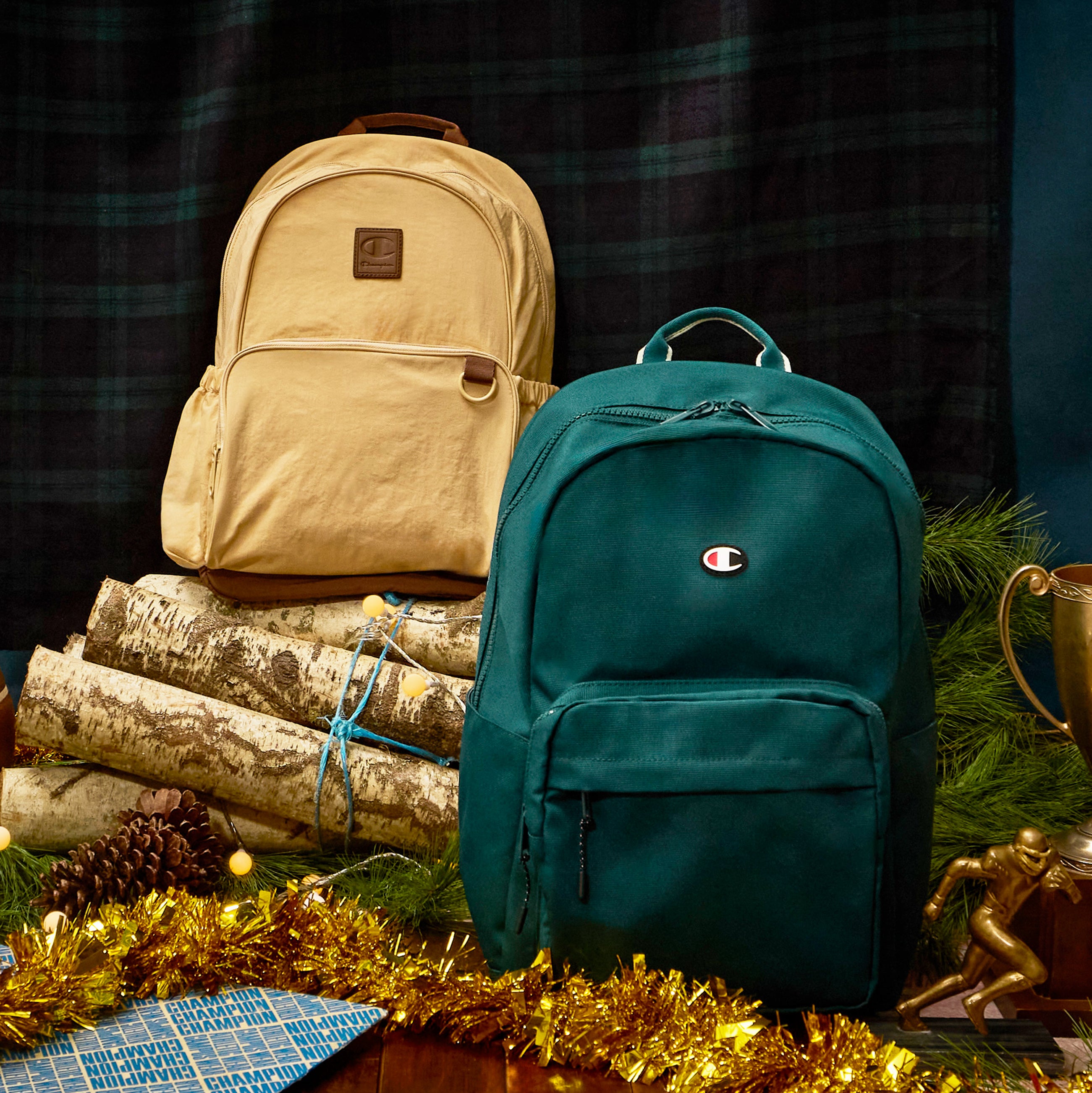 Two backpacks, one beige and one teal, on a decorative background with logs and Christmas decorations.